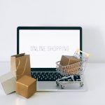 Laptop z napisem Online Shopping, kartonowe pudełka i mały wózek – drogeria internetowa bez magazynu