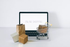 Laptop z napisem Online Shopping, kartonowe pudełka i mały wózek – drogeria internetowa bez magazynu
