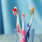 Trzy kolorowe szczoteczki w szklance na niebieskim tle – mycie zębów dziecka