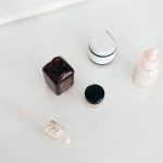 Otwarty flakon serum z pipetą obok słoiczków kremu na białym blacie