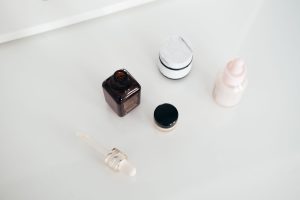 Otwarty flakon serum z pipetą obok słoiczków kremu na białym blacie