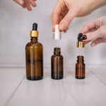 Dłonie trzymające brązowe buteleczki serum z pipetą – witamina C czy kwas hialuronowy