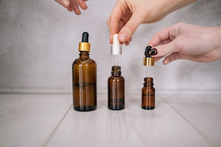 Dłonie trzymające brązowe buteleczki serum z pipetą – witamina C czy kwas hialuronowy